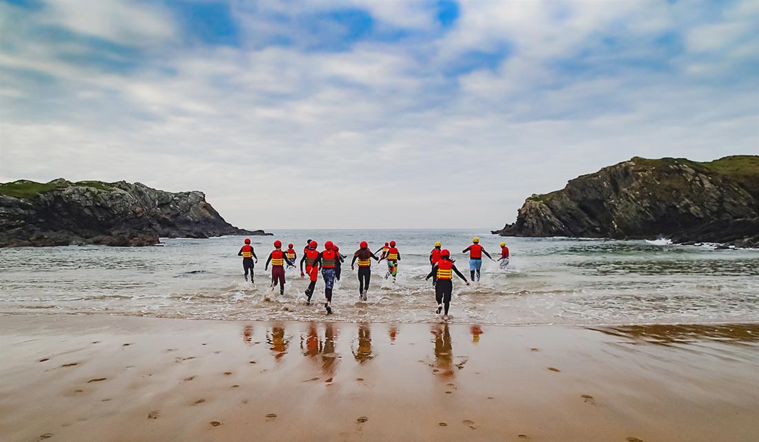 Group of people coasteering running into Porth Dafarch sea water